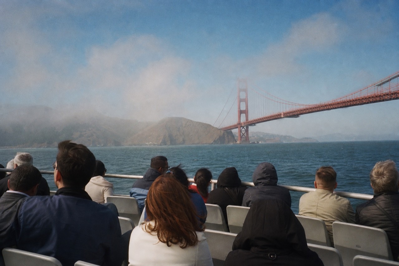 A red-and-white sightseeing boat cutting across the open bay with passengers lined along the rail, the low city skyline bright behind under a clear sky.